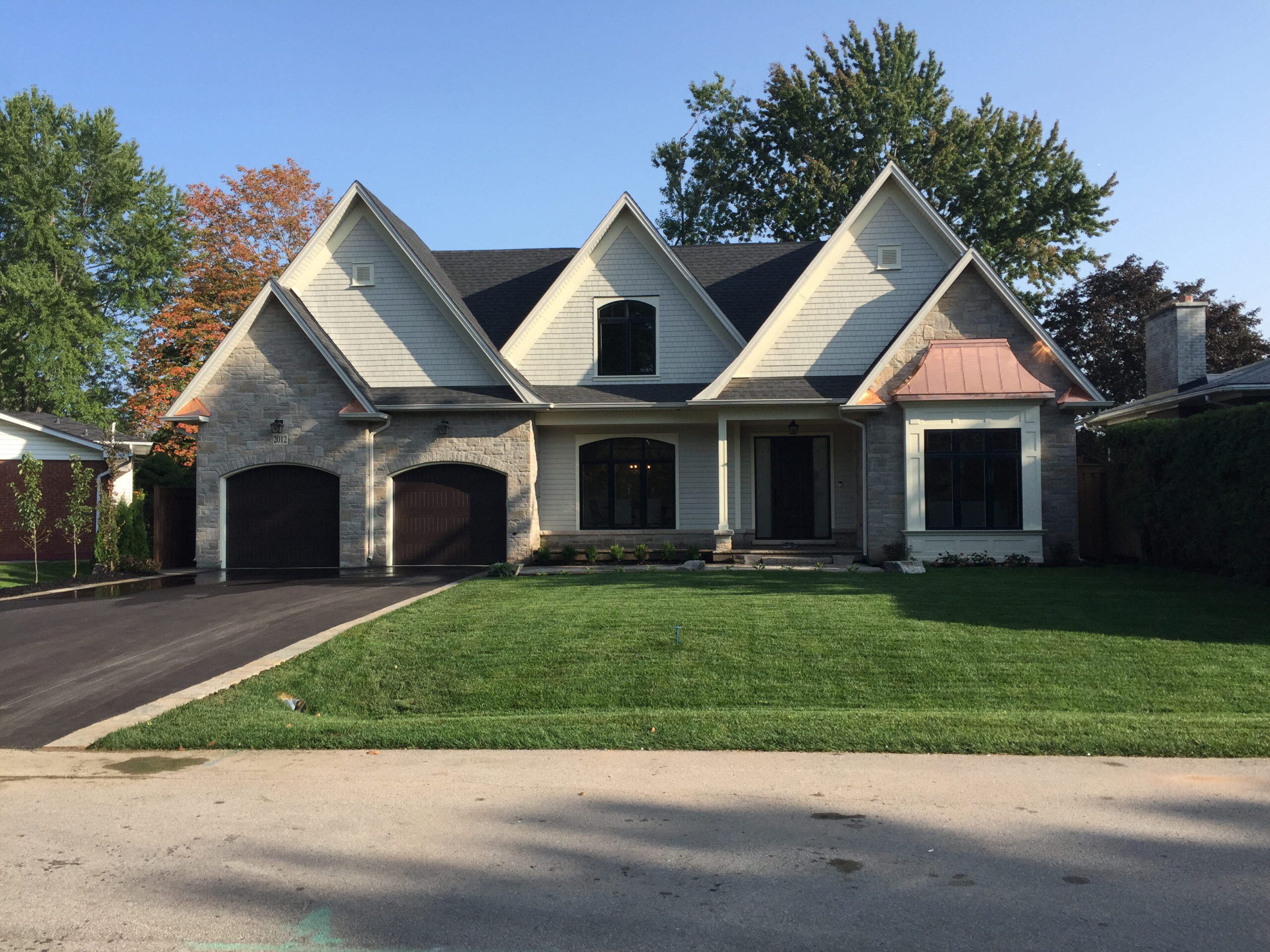 Shingle-style home with steep gables and copper detailing on a landscaped lot