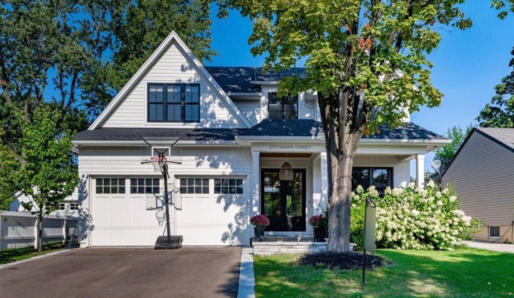 White board-and-batten home with a black-framed front door and mature trees