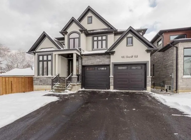 Two-storey stucco and stone home with a double garage and dark-framed windows in winter
