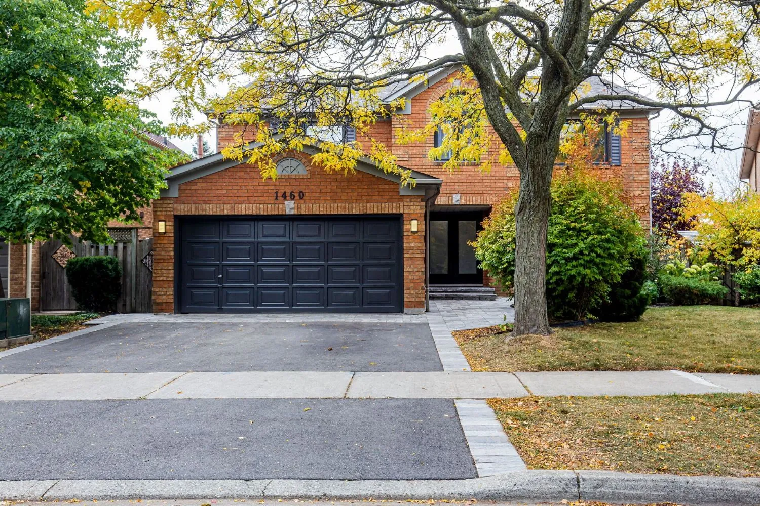 Brick two-storey family home with a black garage door, new interlock walkway and refreshed landscaping